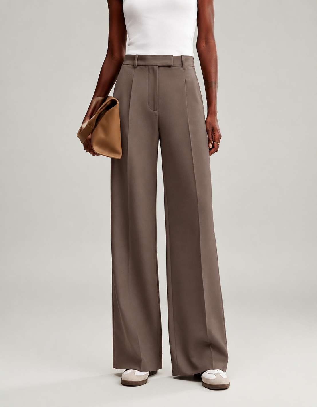 Pantalón marrón topo de corte amplio visto de frente, combinado con un bolso de mano.