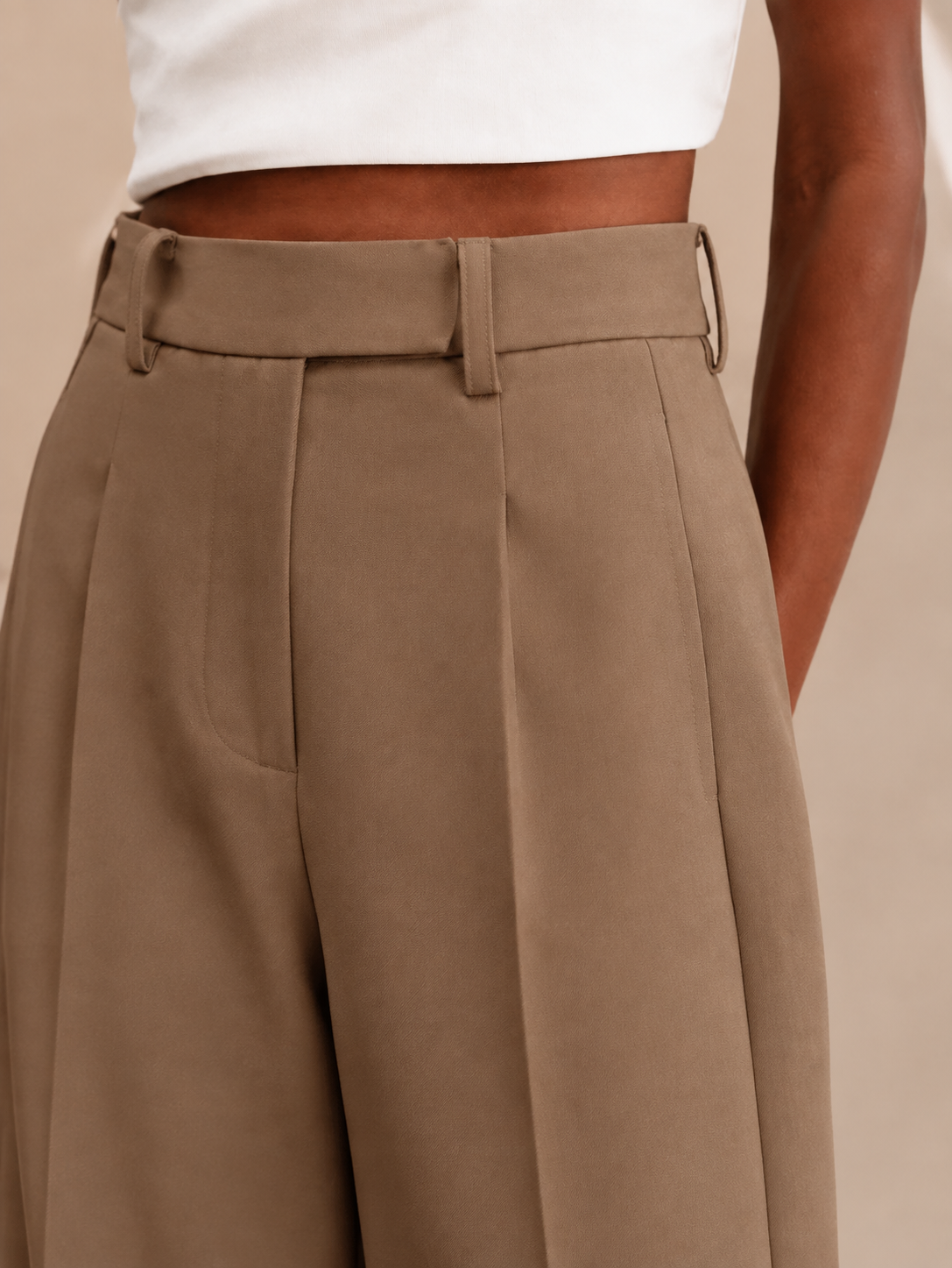 Detalle del pantalón marrón en la cintura, con trabillas, pinzas delanteras y bolsillo lateral.