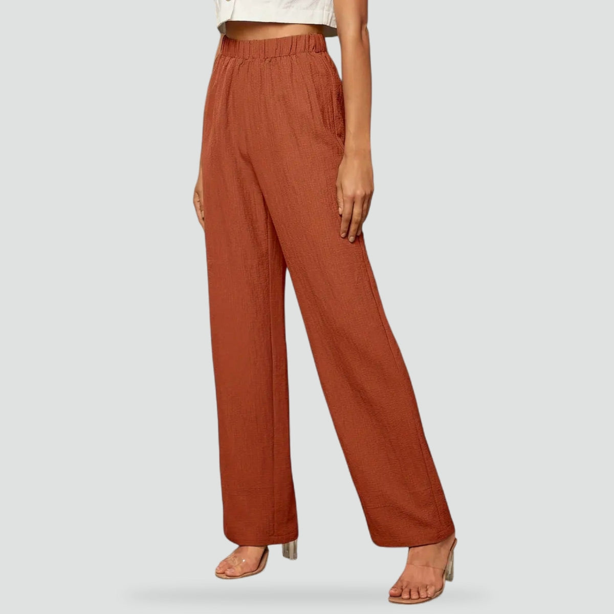 Pantalón de tiro alto en tono terracota, con cintura elástica, pierna recta y bolsillos laterales, visto de frente en un estilismo con sandalias.