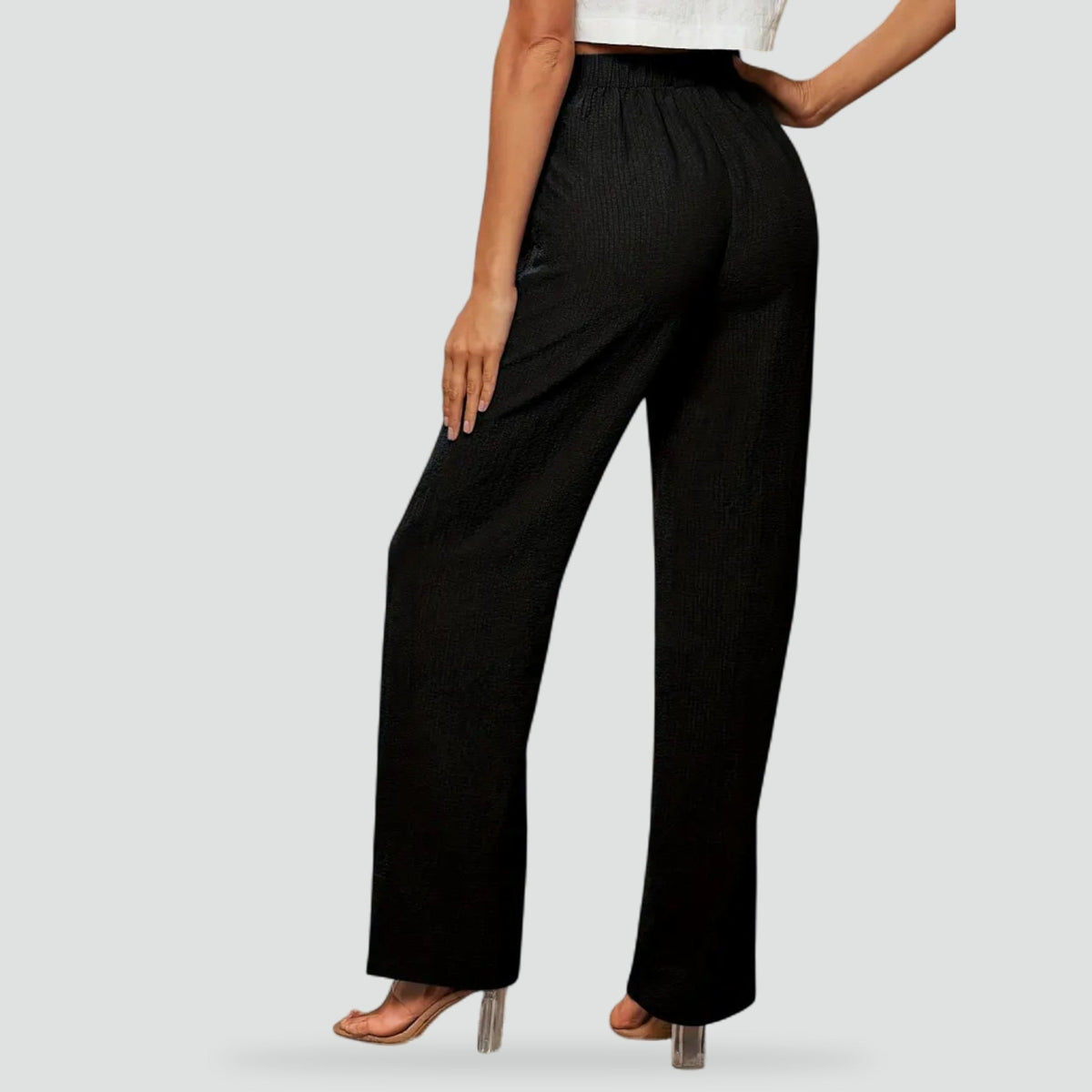 Vista posterior del pantalón negro de cintura alta y pierna recta, combinado con sandalias de tacón.