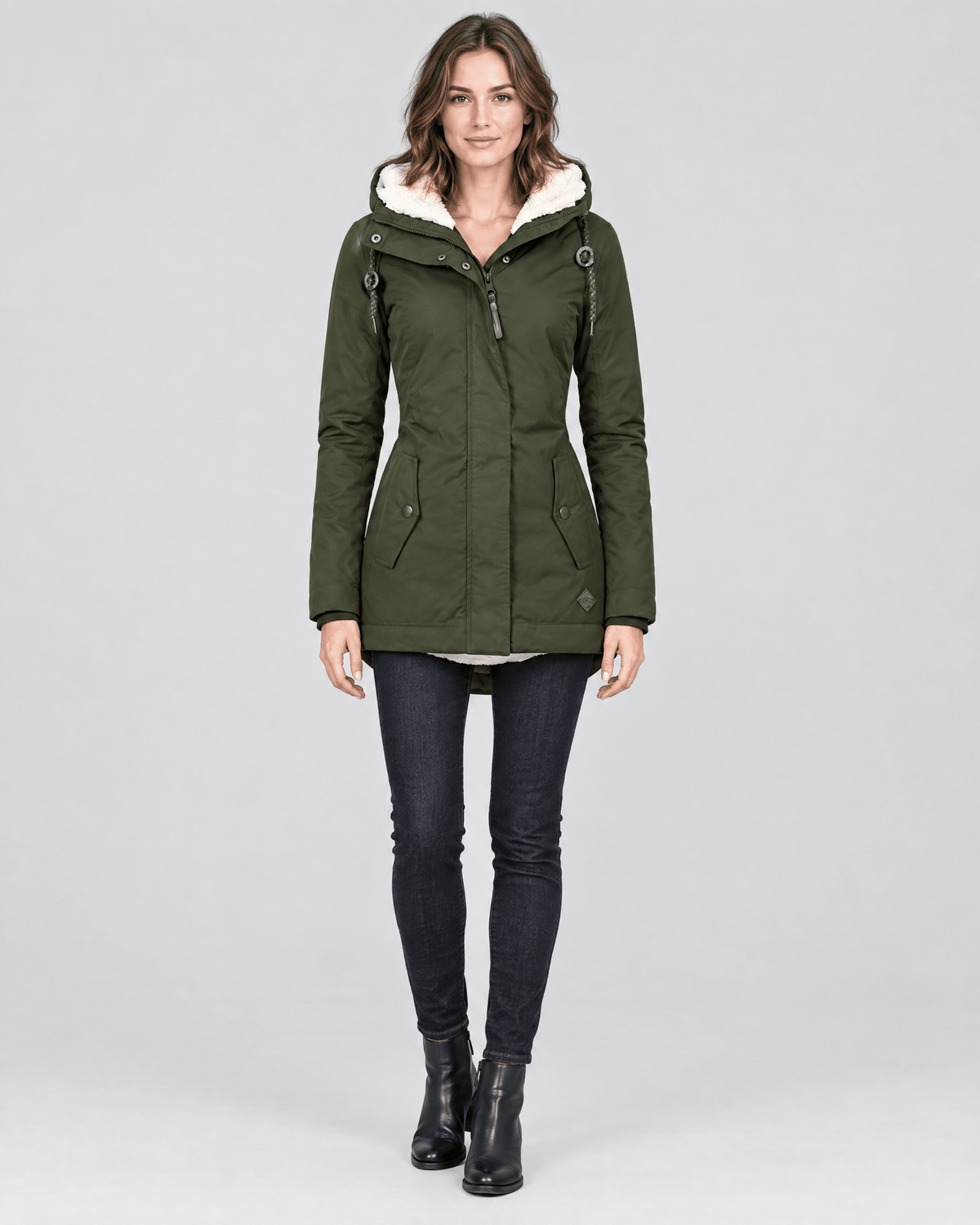 Parka verde oliva entallada con capucha de forro claro, cierre frontal y bolsillos laterales, llevada con vaqueros.