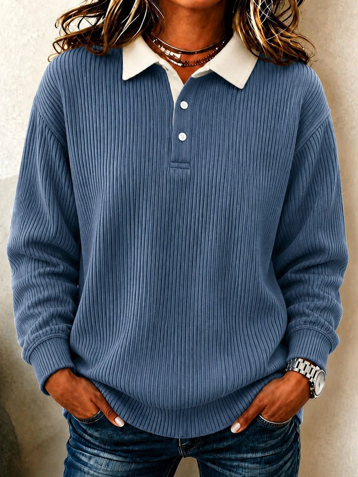 Polo azul grisáceo de manga larga con cuello crema, dos botones y puños acanalados.