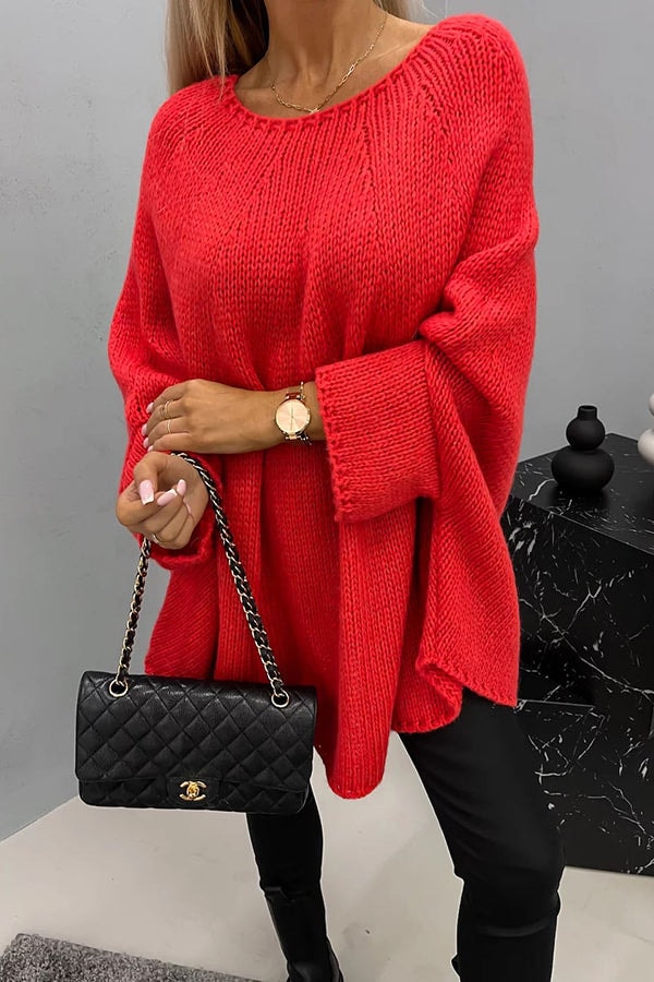 Poncho de punto holgado rojo intenso, de cuello redondo y mangas largas, combinado con pantalones negros y botas.