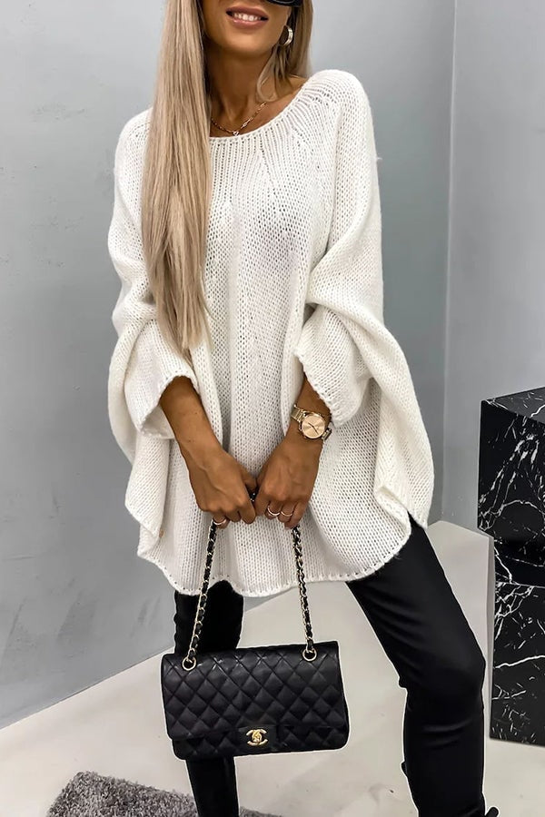 Poncho de punto holgado blanco con cuello redondo, caída amplia y mangas largas, acompañado de un bolso negro y pantalones ajustados.