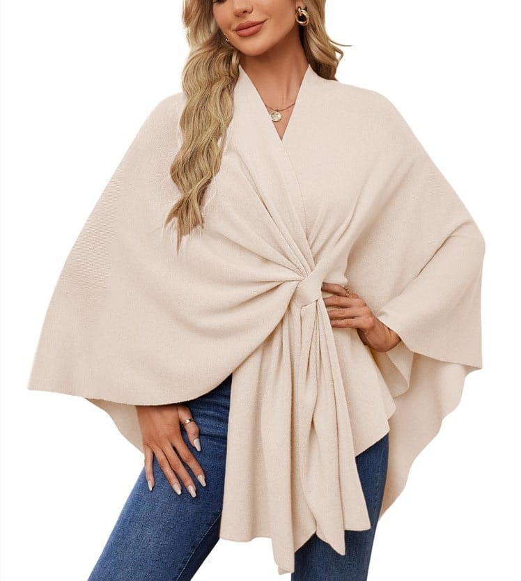 Poncho tipo chal crema con nudo frontal y volumen amplio en los laterales.
