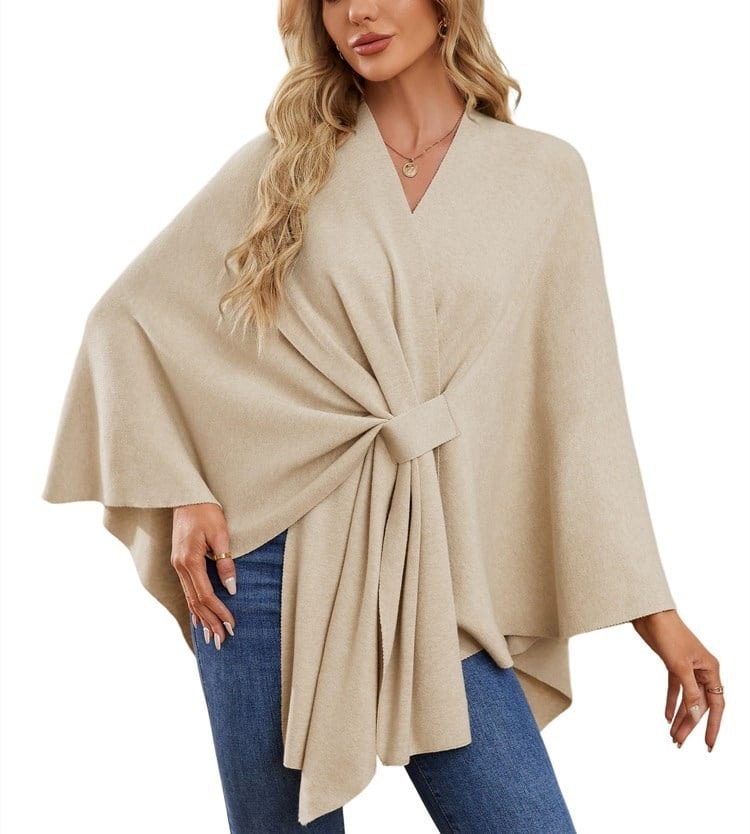 Poncho tipo chal beige arena con banda frontal, corte amplio y un brazo extendido.