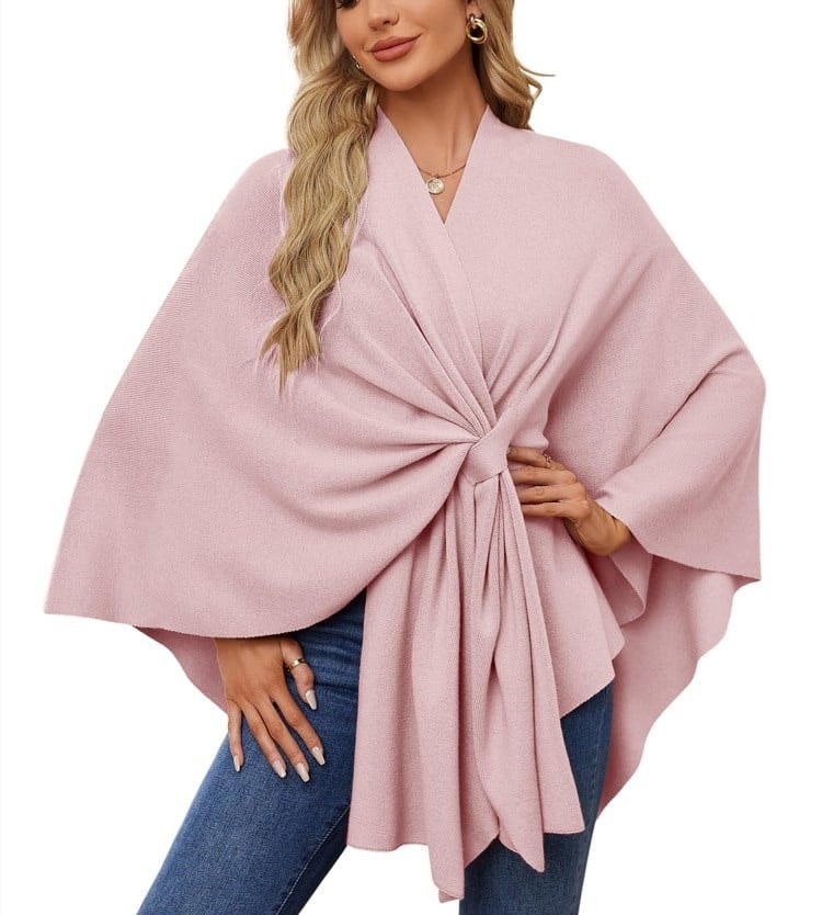 Poncho tipo chal rosa pálido con nudo frontal y pliegues largos que caen sobre el pantalón.