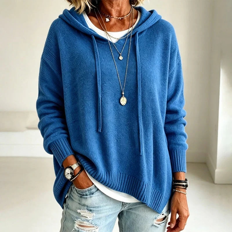 Detalle de la sudadera azul con capucha, cordones largos, bajo acanalado y abertura lateral sobre vaqueros desgastados.