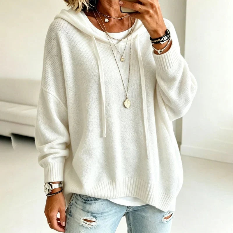 Sudadera blanca con capucha y cordones, de corte holgado, combinada con vaqueros claros desgastados.