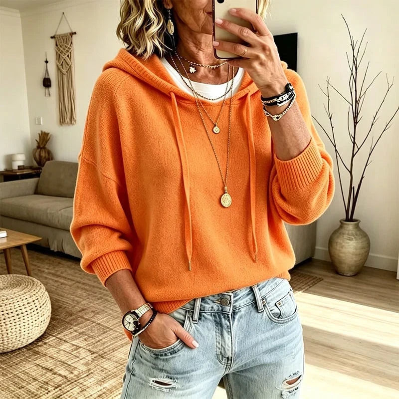 Sudadera naranja con capucha y cordones, combinada con vaqueros desgastados en un interior de estilo acogedor.