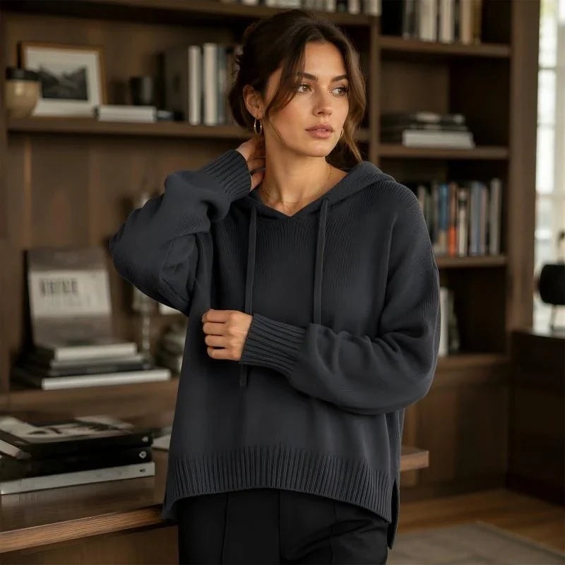 Sudadera negra con capucha y cordones, de mangas amplias y puños acanalados, llevada con pantalón oscuro.