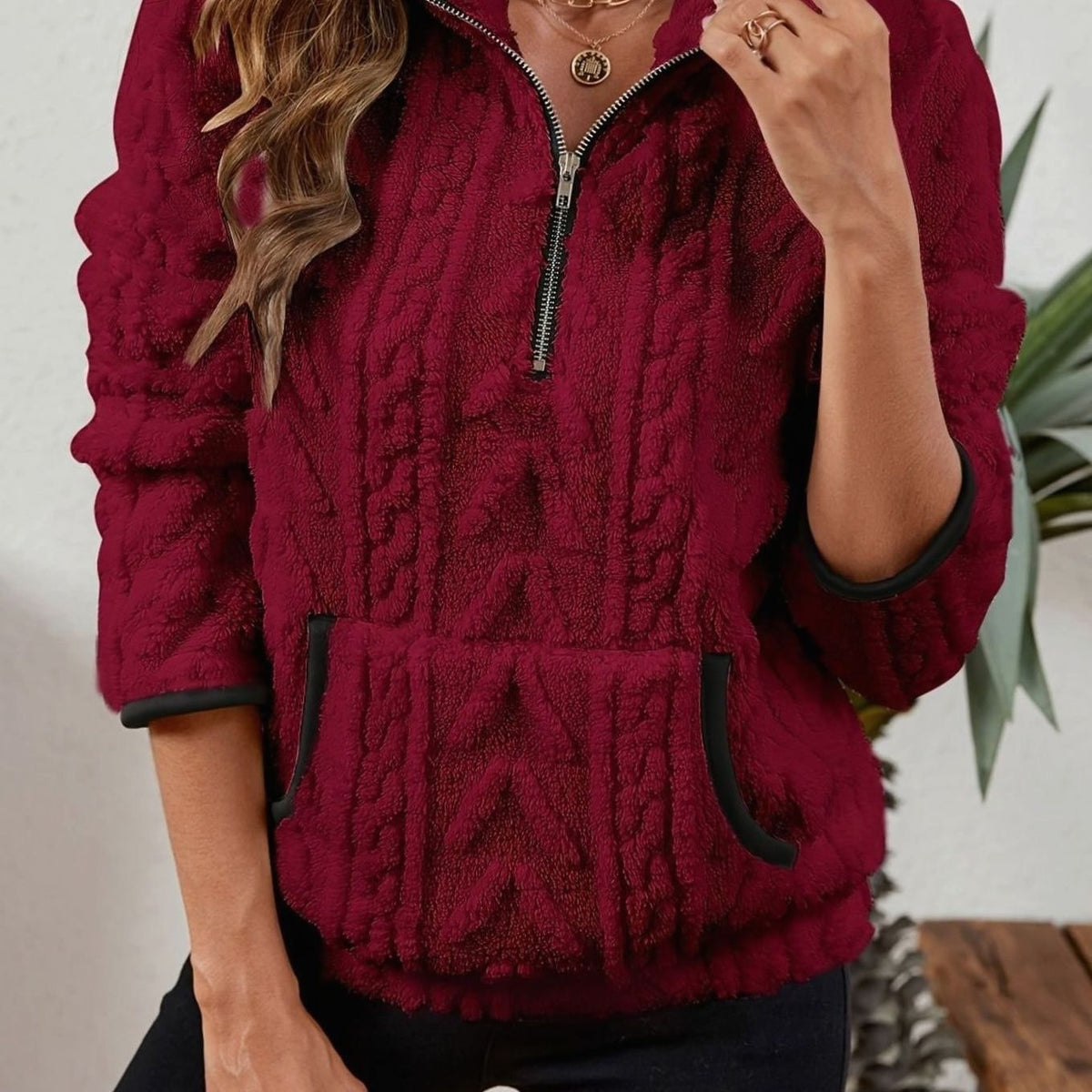 Sudadera burdeos de cuello alto con cremallera parcialmente abierta, textura en relieve y bolsillo canguro.