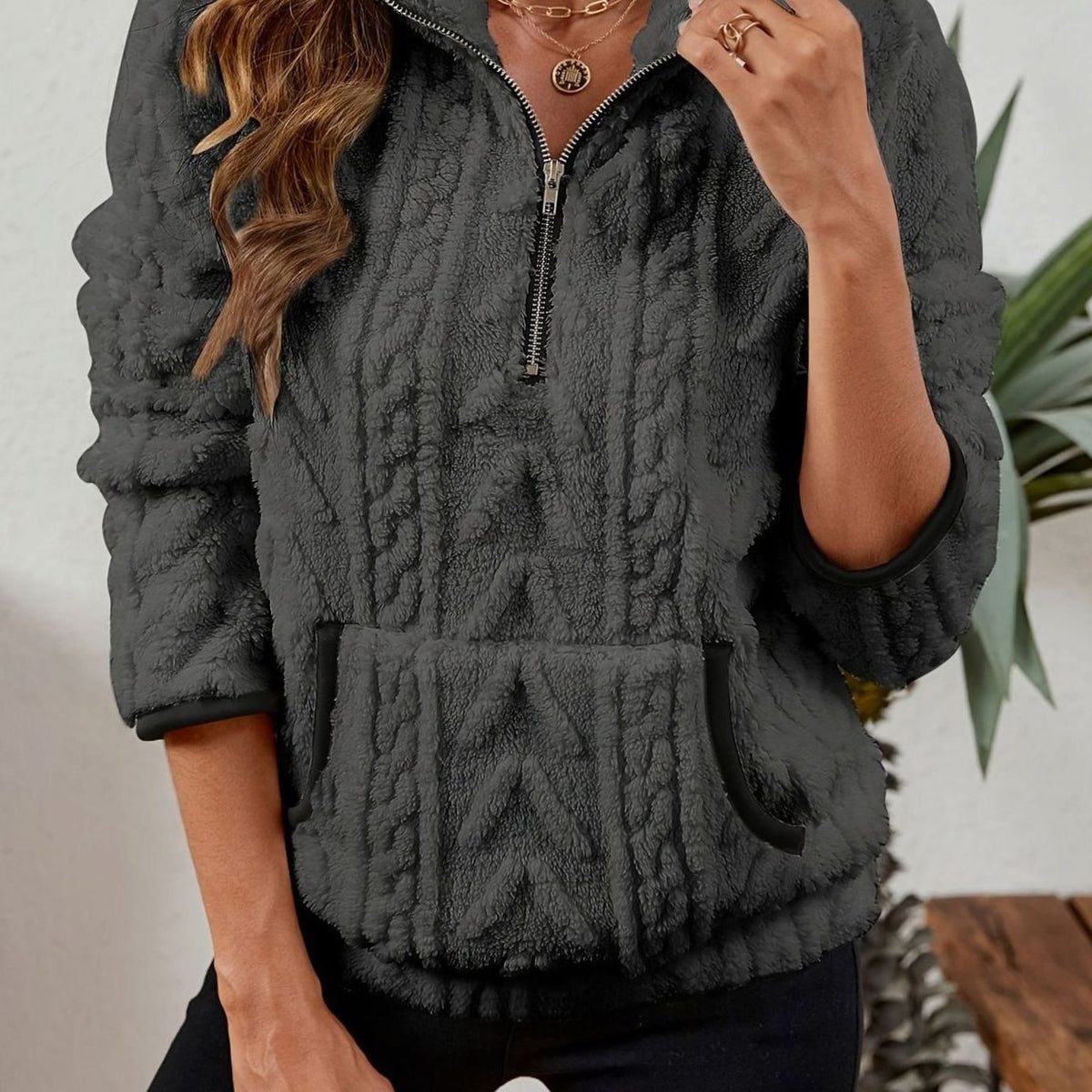 Sudadera gris oscuro con cuello alto, cremallera corta, puños oscuros y bolsillo canguro.