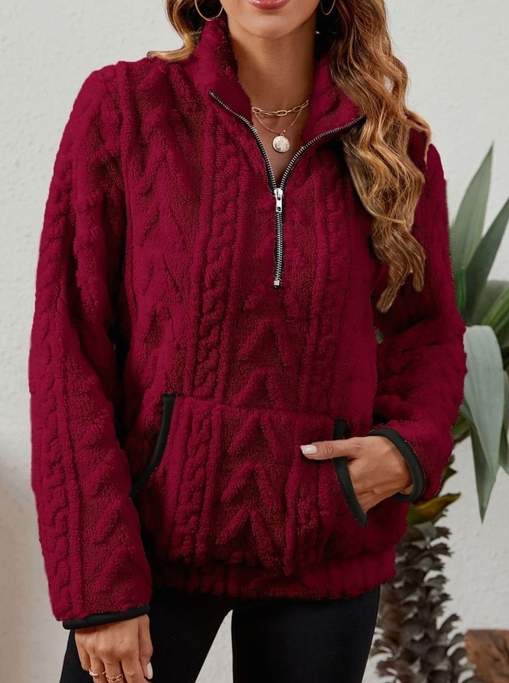 Detalle frontal de la sudadera burdeos con cuello elevado, cremallera corta y ribetes oscuros en el bolsillo.