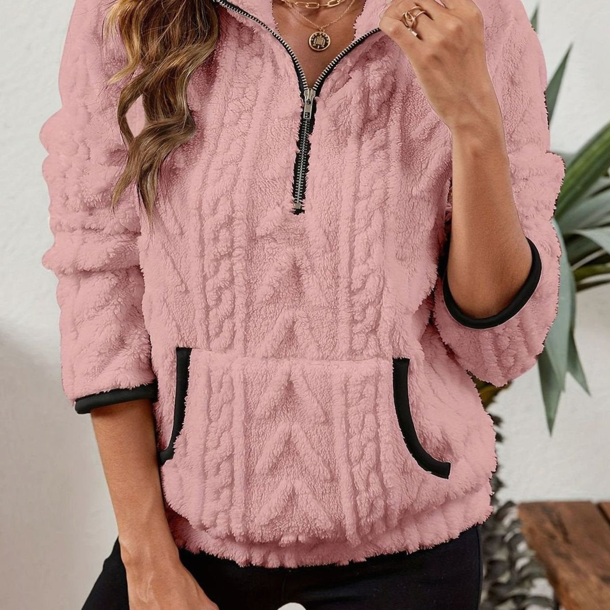 Sudadera rosa claro con mangas largas, cuello alto con cremallera y bolsillo canguro de bordes oscuros.