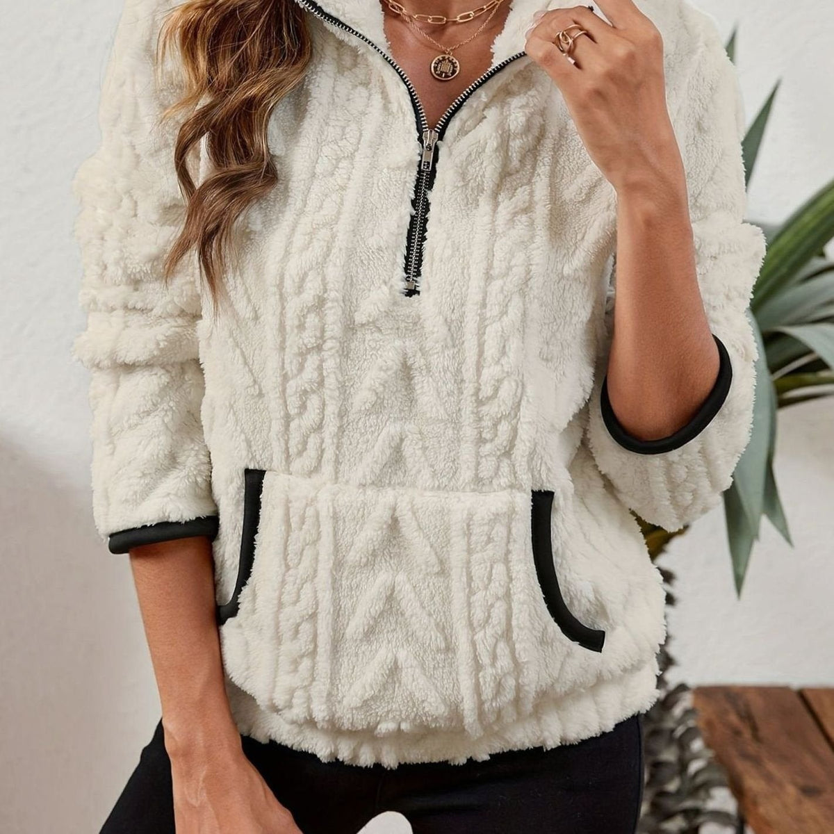 Sudadera blanca de cuello alto con cremallera frontal, textura en relieve y bolsillo canguro.