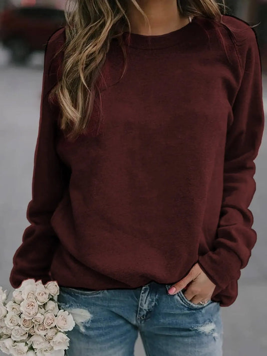 Sudadera burdeos de cuello redondo y mangas raglán, combinada con vaqueros y un ramo de flores.