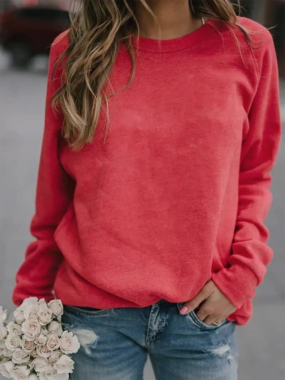 Sudadera roja de corte relajado, cuello redondo y mangas raglán, con vaqueros desgastados.