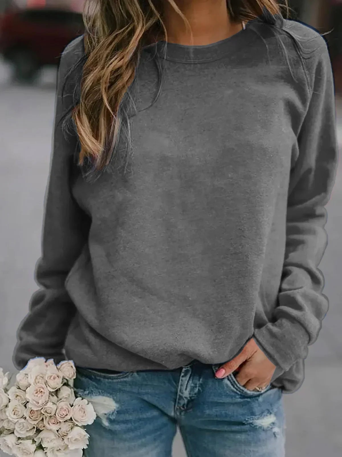 Sudadera gris de cuello redondo con mangas raglán y puños ceñidos, en un conjunto informal.