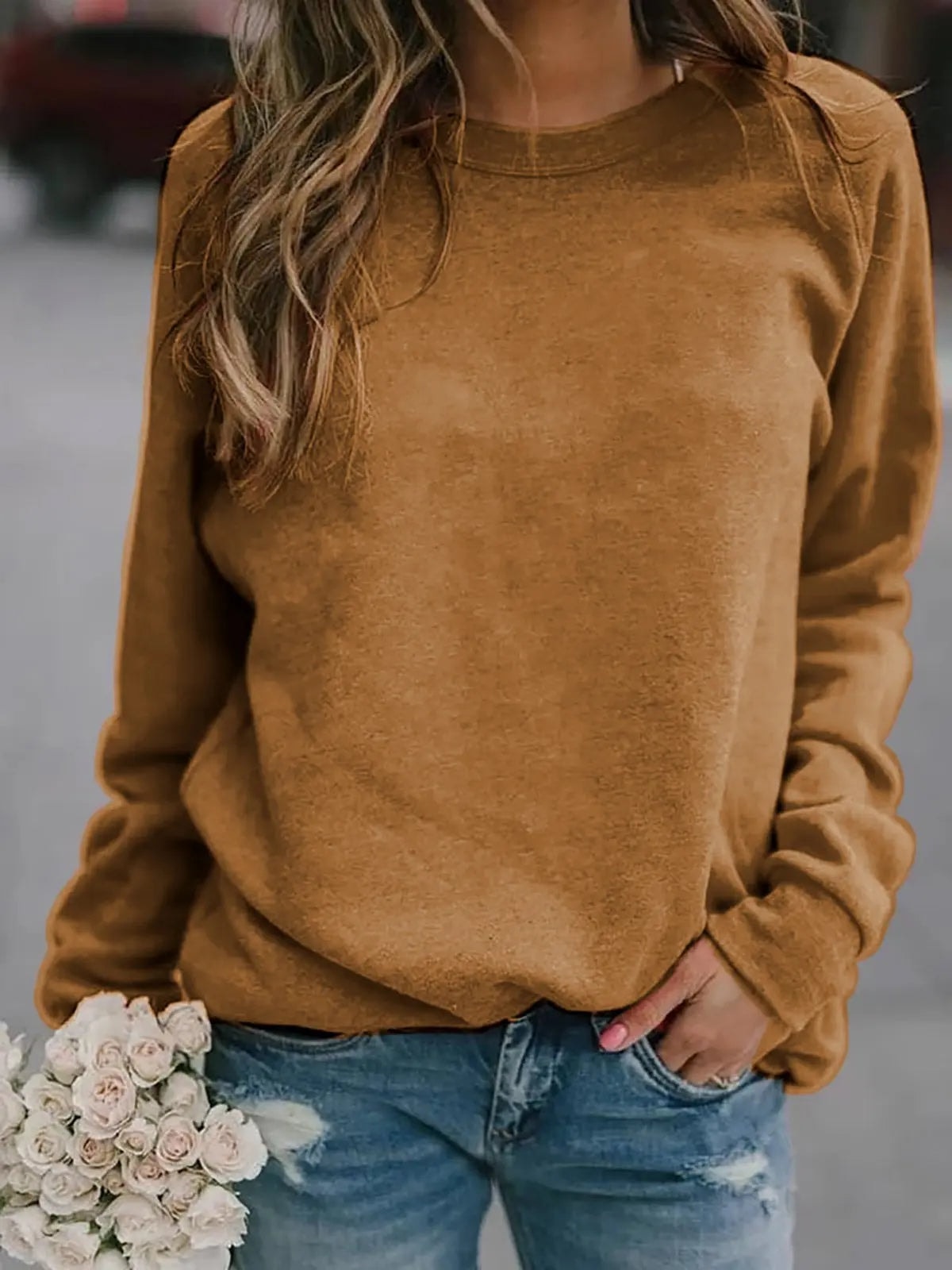 Sudadera marrón de cuello redondo y mangas raglán, combinada con vaqueros y flores claras.