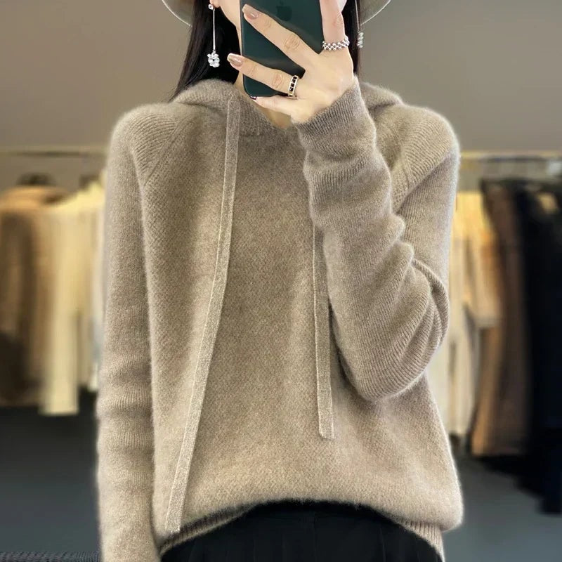 Sudadera de punto oversize en tono topo, con capucha y cordones largos, combinada con pantalón negro.