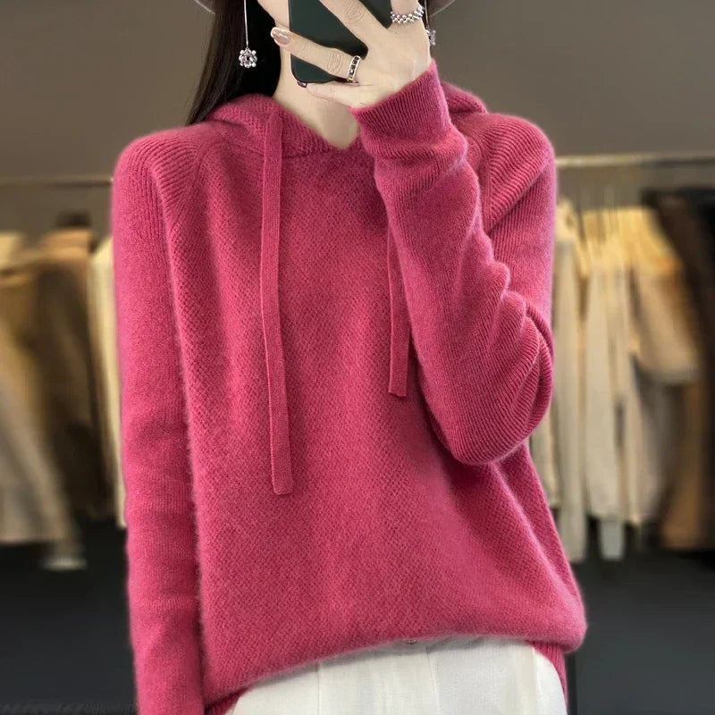 Sudadera de punto oversize rosa fucsia con capucha y cordones, llevada sobre un pantalón claro.
