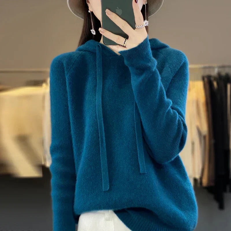 Sudadera de punto oversize azul petróleo con capucha y cordones, combinada con una prenda inferior clara.