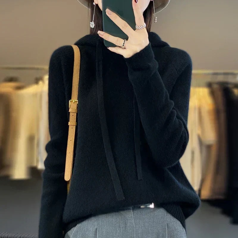 Sudadera de punto oversize negra con capucha y cordones, acompañada de pantalón gris y bolso al hombro.