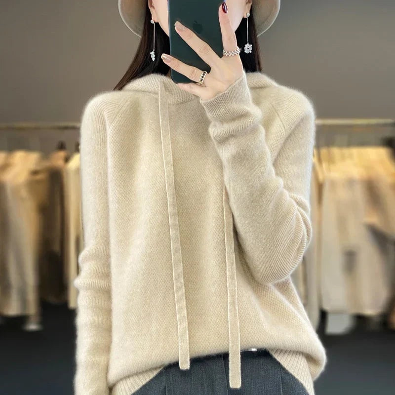 Sudadera de punto oversize color crema con capucha y cordones largos, sobre un pantalón oscuro.