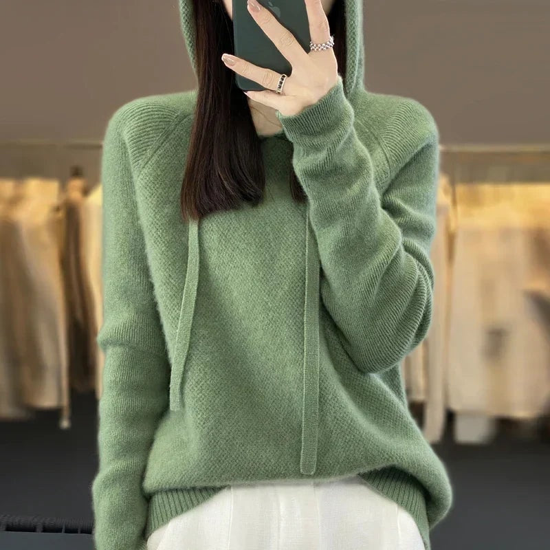 Sudadera de punto oversize verde salvia con capucha y cordones, llevada con pantalón blanco.