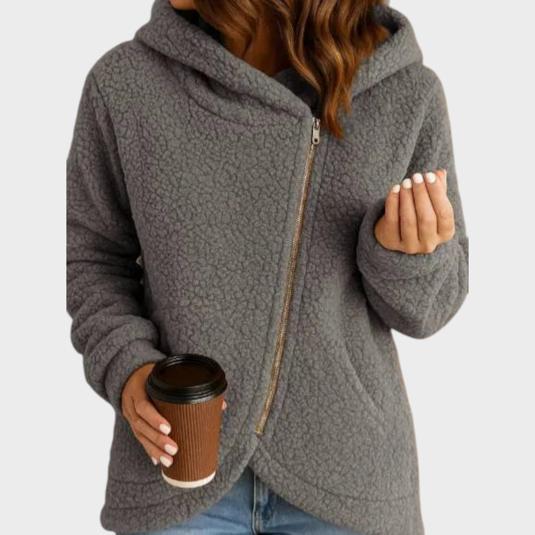 Sudadera holgada gris con capucha envolvente y cremallera asimétrica, combinada con vaqueros.