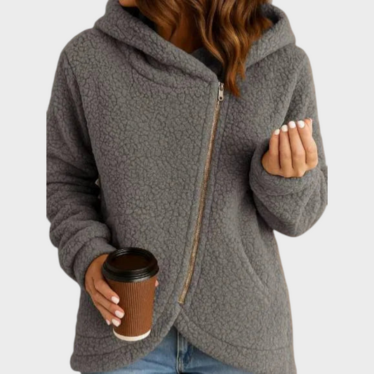 Sudadera holgada gris con capucha envolvente y cremallera asimétrica, combinada con vaqueros.