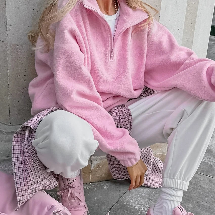 Detalle de la sudadera rosa con cuello alto y media cremallera mientras se lleva con pantalones claros en un conjunto relajado.