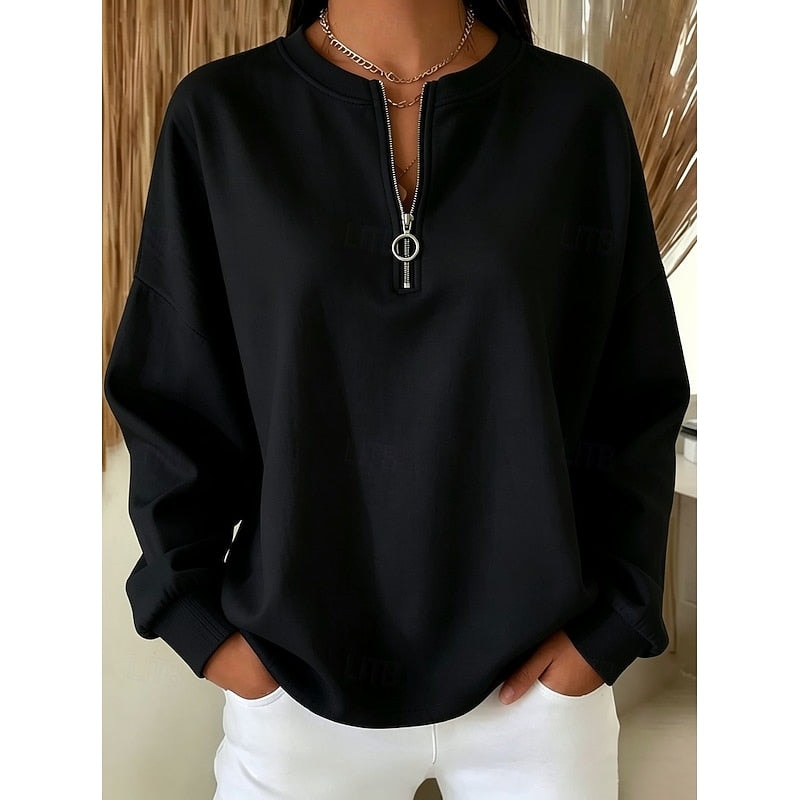 Sudadera holgada negra con media cremallera frontal y tirador de aro, llevada con pantalón blanco.