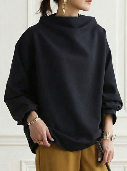 Sudadera negra holgada con cuello alto, mangas largas amplias y bajo redondeado, combinada con pantalón mostaza.