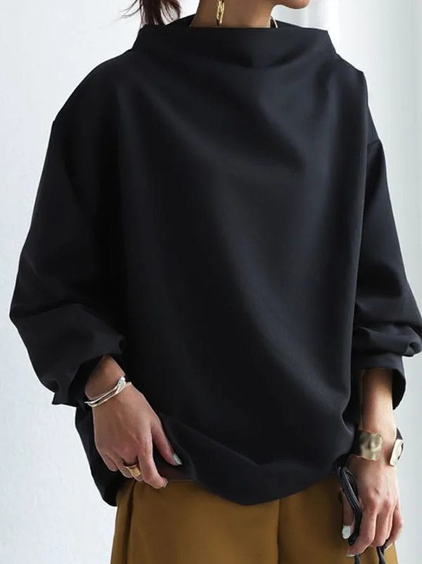 Primer plano frontal de la sudadera negra con cuello alto amplio, volumen holgado y mangas largas recogidas.