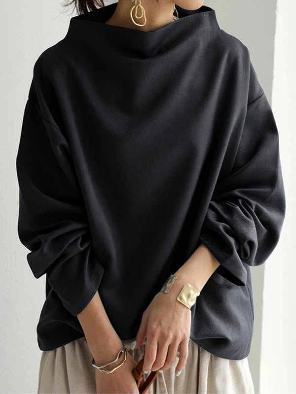 Vista frontal de la sudadera negra con cuello alto y mangas abullonadas recogidas, combinada con pantalón claro.