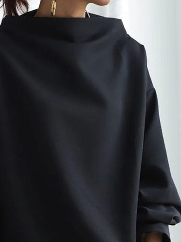 Detalle cercano del cuello alto y la manga larga de la sudadera negra, mostrando su silueta amplia.
