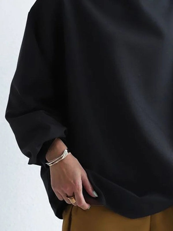 Detalle del bajo redondeado y la manga amplia de la sudadera negra holgada, con el puño recogido.
