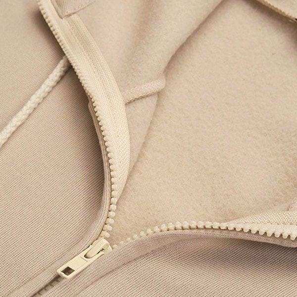 Detalle cercano de la cremallera frontal y el interior de la capucha de la sudadera beige.