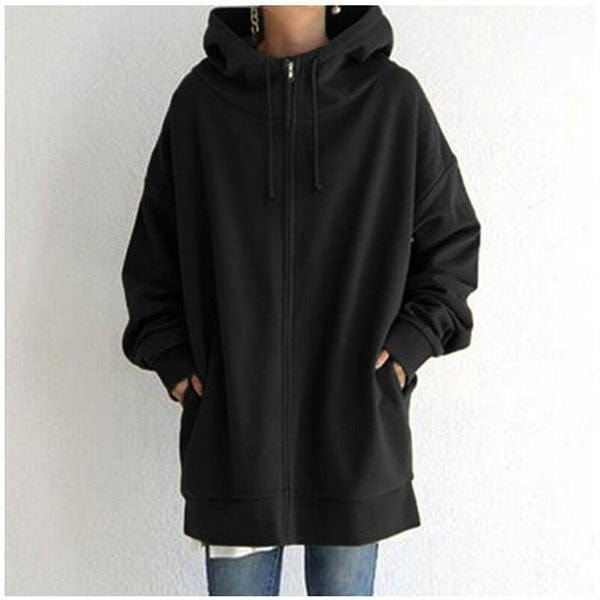 Sudadera oversize negra con capucha, cordones y cremallera frontal, mostrada de frente con ambos bolsillos ocupados.