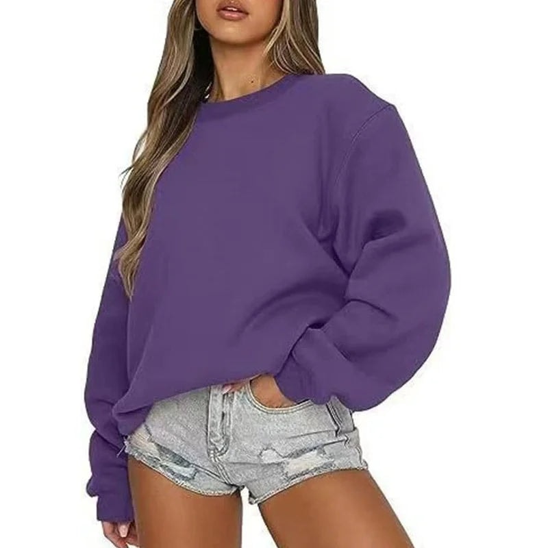 Sudadera oversize morada de cuello redondo y corte desenfadado, combinada con shorts claros.