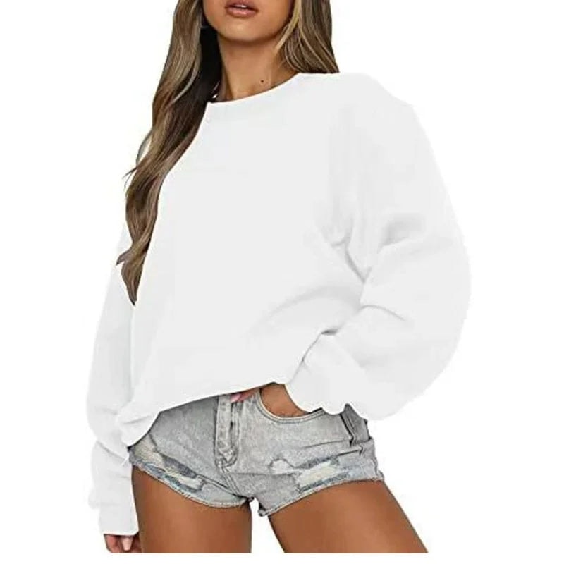 Sudadera oversize blanca de cuello redondo, mostrada con el bajo ligeramente recogido sobre shorts.