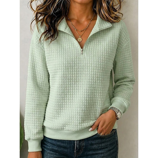 Sudadera texturizada verde claro con cuello y media cremallera, mangas largas y acabados acanalados, combinada con vaqueros oscuros.