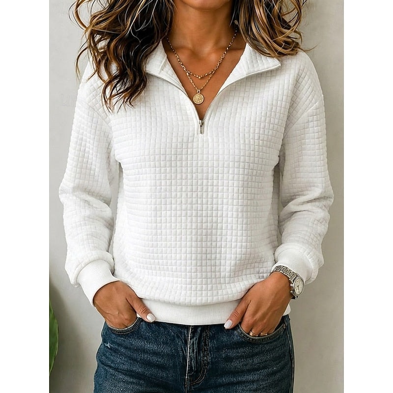Sudadera texturizada blanca con media cremallera abierta, cuello elevado y puños acanalados, llevada con las manos en los bolsillos de unos vaqueros.