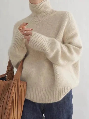 Vista frontal de un suéter beige de cuello alto, bajo y puños acanalados, llevado con vaqueros oscuros.