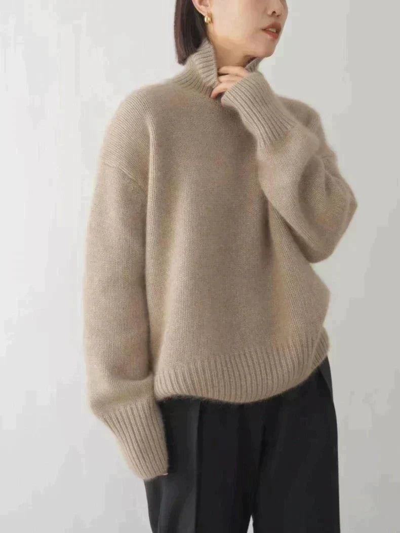 Vista lateral de un suéter beige de cuello alto con mangas largas y bajo acanalado, combinado con pantalón negro.