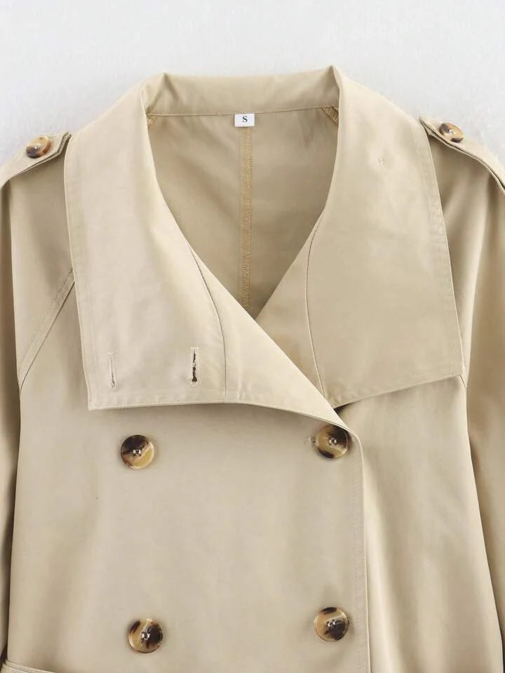 Primer plano de la parte superior del trench beige, con cuello amplio, doble botonadura y detalles de los hombros.