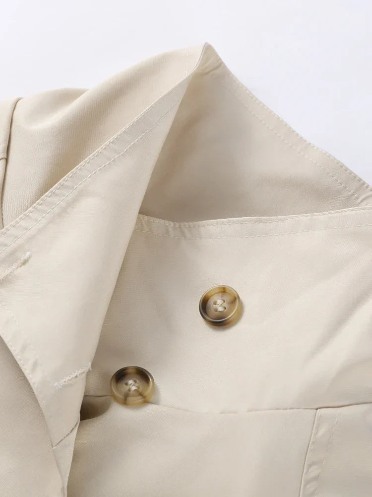 Detalle del cuello alto y las solapas del trench beige, con dos botones visibles en la parte superior.