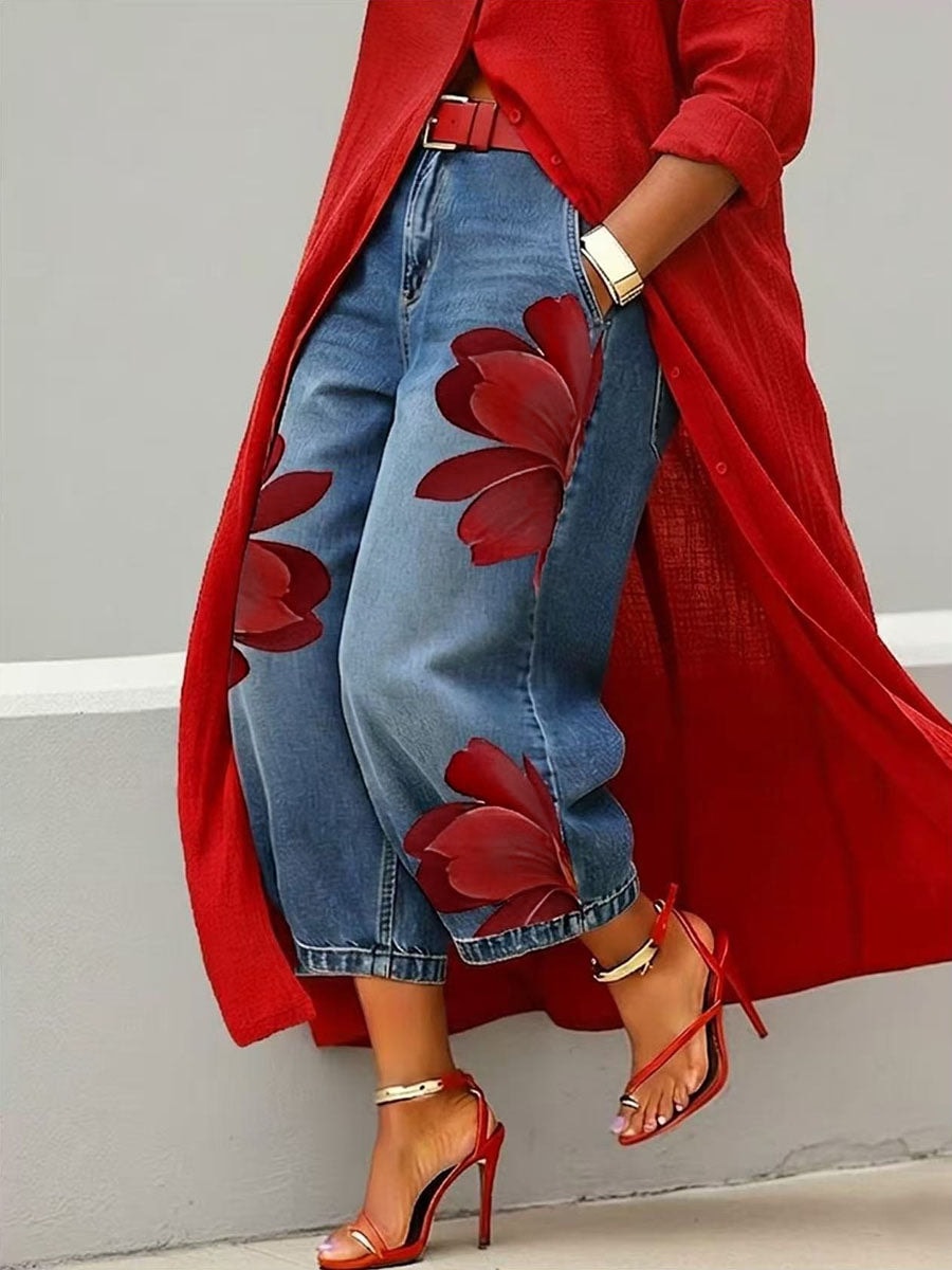 Vaqueros azules de pierna ancha con flores rojas de gran tamaño, vistos de cerca con el bajo por encima del tobillo.